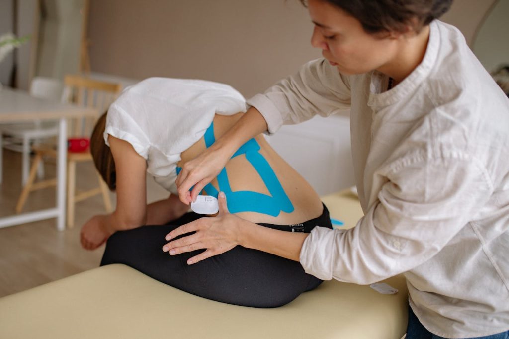 A therapist applies blue kinesiology tape to a patients back in a clinical setting.
